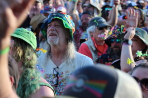 Bearded man wearing a bright rainbow hat among a dense crowd at a festival turnout.