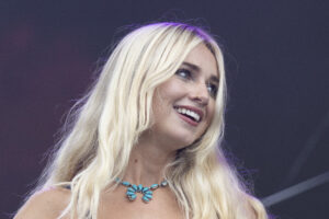 Smiling blonde woman wearing a turquoise necklace on stage with a dark background