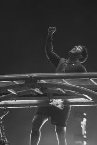 Male performer on stage raising a clenched fist in triumph against a dark background.