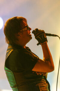 Singer performing onstage, close-up profile with microphone and glove, colorful stage lighting behind him.