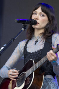 Female singer on stage, close-up with microphone and acoustic guitar.