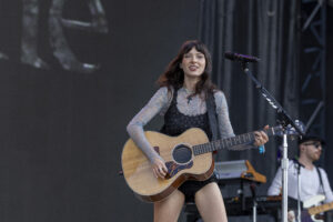 Female guitarist on stage, singing into a microphone while playing an acoustic guitar.