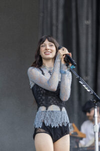 Female singer on stage, wearing a blue lace dress, holding a microphone and smiling during a performance.