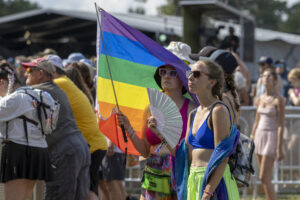 Paradegoers at a Pride event, holding a large rainbow flag with bright outfits and sunglasses in the foreground.