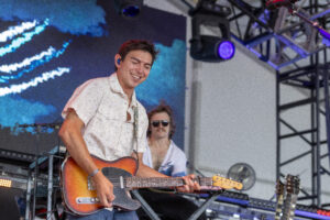 Male guitarist smiling while playing a sunburst electric guitar on stage.
