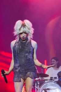 Female singer on stage in a silver sequin dress, holding a microphone under pink stage lights.