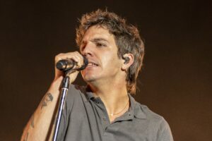 Male singer on stage, close-up, holding a microphone near his mouth with an in-ear monitor visible in his ear