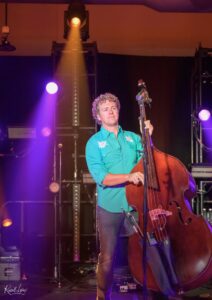 Musician playing a double bass on a dimly lit stage with purple and orange lights in the background.