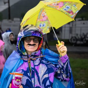 Woman wearing a bright, patterned rain jacket and glasses, holding a yellow umbrella with SpongeBob and cartoon designs.