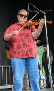 Violinist wearing sunglasses and a red palm-print shirt plays violin on stage.