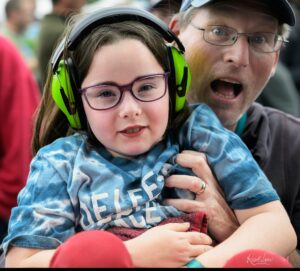 Close-up of a girl wearing neon green over-ear headphones, with a man wearing glasses behind her.