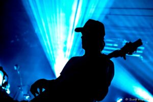Silhouette of a person wearing a cap on stage with intense blue lighting behind them at a concert.