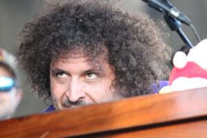 Close-up of a man with curly dark hair peeking over a wooden podium, microphone above him.