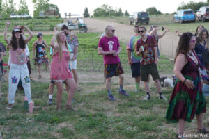 Group of people dancing outdoors at a festival, wearing colorful tie-dye clothing and summer outfits.
