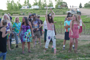 Group of people in tie-dye clothing enjoying an outdoor festival, some with arms raised.