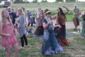 Group of people dancing outdoors in a grassy area, wearing colorful maxi dresses and casual summer clothes.
