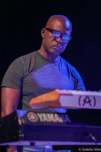 Male musician wearing glasses, playing a Yamaha keyboard on stage under blue lights.