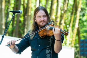 Male violinist playing outdoors with a microphone nearby, forest background and sunlight filter through trees