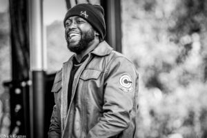 Black-and-white portrait of a smiling man wearing a beanie and a jacket outdoors.