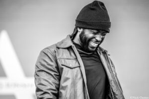 Smiling man wearing a knit black beanie and jacket, looking down in a candid moment (black and white).