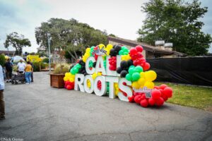 Large colorful balloon sculpture spelling 'CAL ROOTS' at an outdoor festival with people and tents in the background