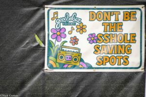 Colorful retro-style sign on dark fabric advertising a show or event, reading 'DON'T BE THE SHOE SAVING SPOTS' with flowers and a boombox illustration (posed banner).
