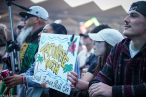 Crowd of young people at an outdoor event holding a colorful poster reading 'Fortunate Youth'.