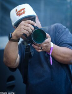 Photographer aiming a camera with a large lens, wearing a white cap and blue shirt.