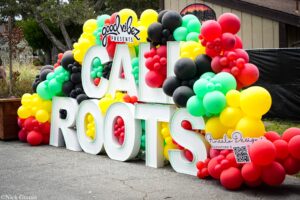 Vibrant balloon sculpture surrounding large white letters forming a sign, with 'Good Vibes Presents' at top.