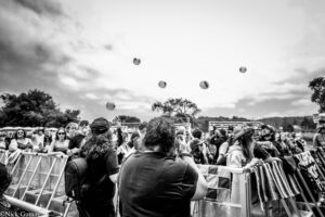 Crowd of people behind metal barriers at an outdoor event, balloons floating in the sky above.