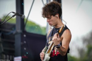Young guitarist playing an electric guitar on stage, near a microphone, focused on the fretboard.