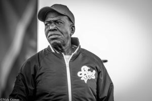 Black-and-white portrait of an older man wearing a cap and zipped jacket, looking off to the side with a serious expression.