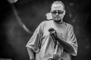 Male singer wearing sunglasses grips a microphone on stage, focused on performing (black-and-white photo).
