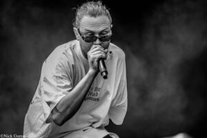 Male singer wearing sunglasses, gripping a microphone and performing on stage (black and white)