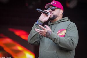 Male singer in a pink cap and sunglasses performs on stage, holding a microphone close to his mouth.