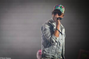 Singer wearing a colorful tropical cap and sunglasses, holding a microphone on stage.