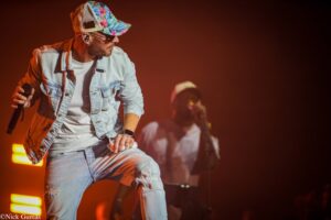 Male singer on stage wearing a floral cap and light denim jacket, holding a microphone during a live performance.
