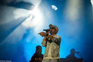 Male singer on a smoky blue-lit stage, wearing sunglasses and a floral cap, holding a microphone and performing.