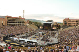 Overflowing outdoor stadium filled with concertgoers facing a large stage with screens and lights.
