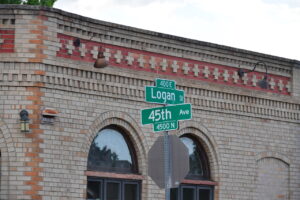 Green street signs reading Logan St and 45th Ave mounted on a metal post in front of a brick building.