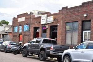 Brick storefront with bar and cocktail signs, neon OPEN sign, and several parked cars along the street.
