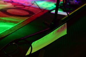 Close-up of a stage with colorful lighting, a microphone stand and a setlist on a sheet of paper nearby