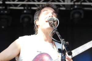 Male guitarist and vocalist performing live, singing into a microphone with a guitar visible on stage