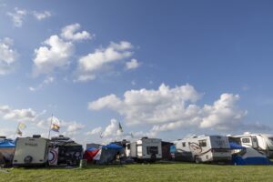 Row of RVs and tents at a sunny campsite, colorful flags fluttering against a blue sky with white clouds.