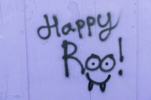 Green spray-painted word 'happy' on a purple wooden wall, with part of a smiling cartoon face visible at the bottom right.