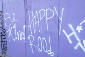 Purple wooden wall with white graffiti tags and cursive lettering (street art).