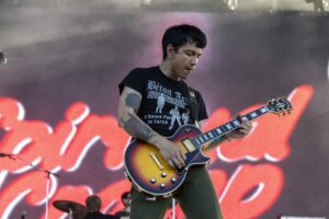 Male guitarist playing a sunburst Les Paul-style guitar on stage with red lights in the background, immersed in the performance.