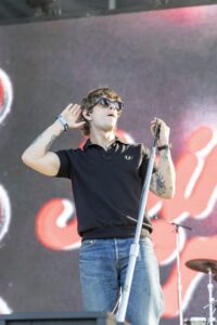 Male singer wearing sunglasses and a black polo on stage, holding a microphone stand.