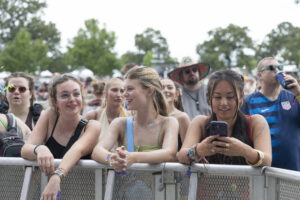 Crowd of young festival attendees leaning on a metal barrier, smiling and looking toward the stage.