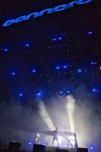 DJ on a glowing metallic platform, surrounded by blue stage lights and thick fog.